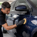 Persona aplicando cera con una almohadilla sobre la carrocería limpia de un coche azul oscuro.