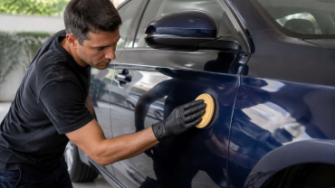 Persona aplicando cera con una almohadilla sobre la carrocería limpia de un coche azul oscuro.