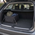 Organizador de tela sujeto en el maletero de un coche, con una mochila pequeña y una chaqueta doblada.